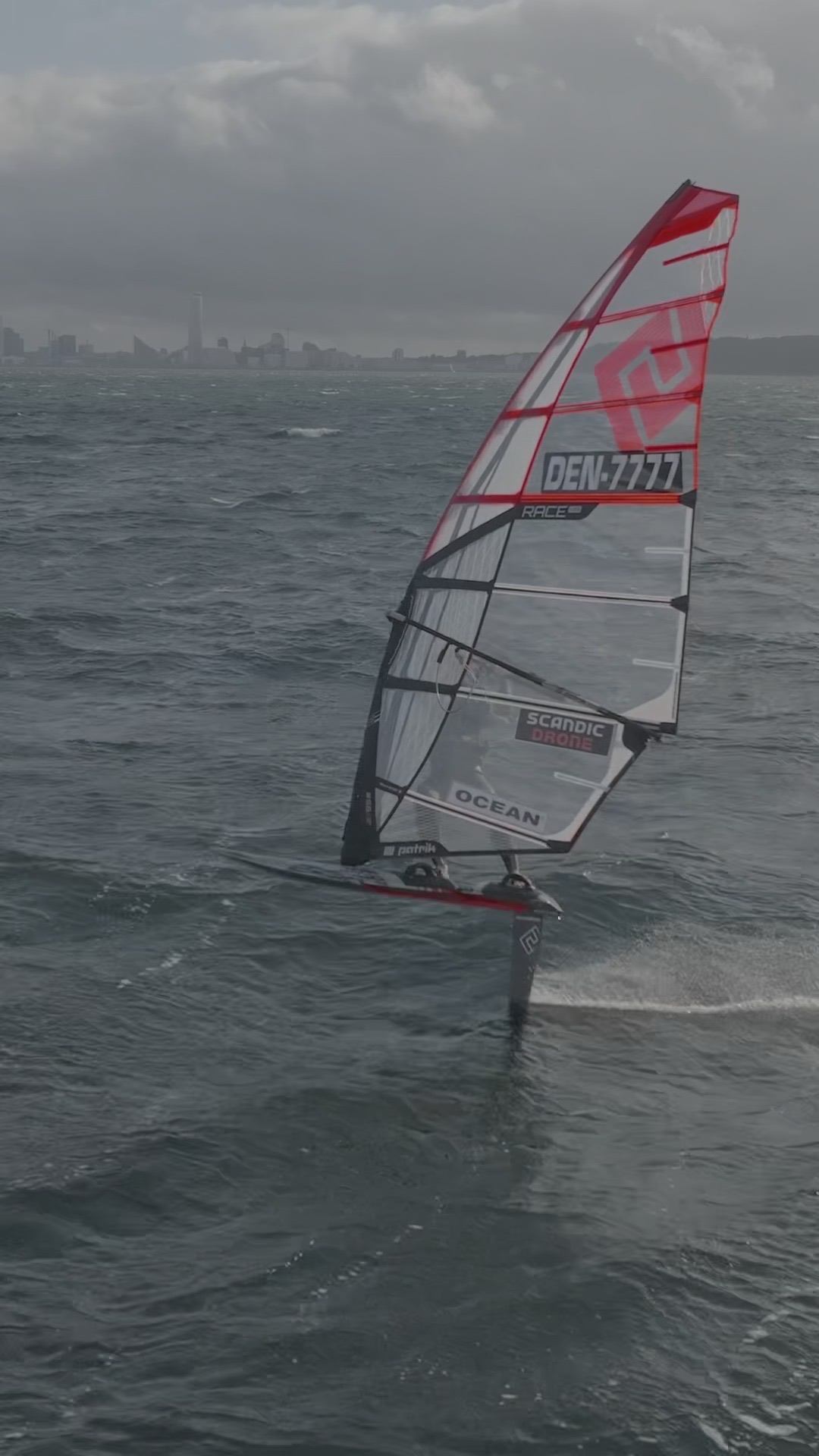 Windsurfer på foil med byen i baggrunden, fotograferet med drone